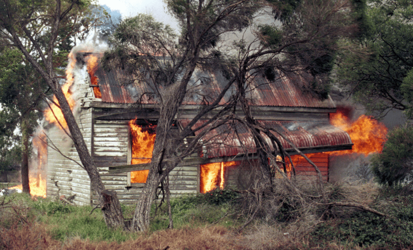 An old white house in the bush burning