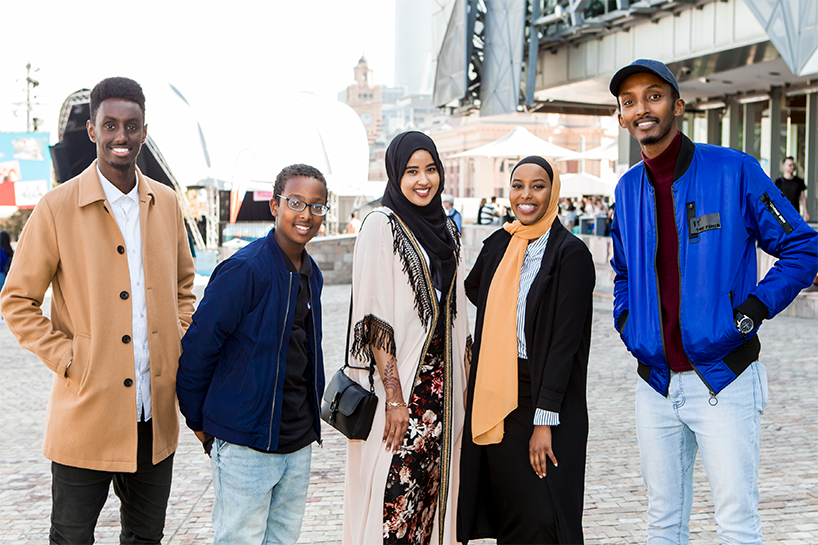 Five young people of African background stand together. Three males and two females.