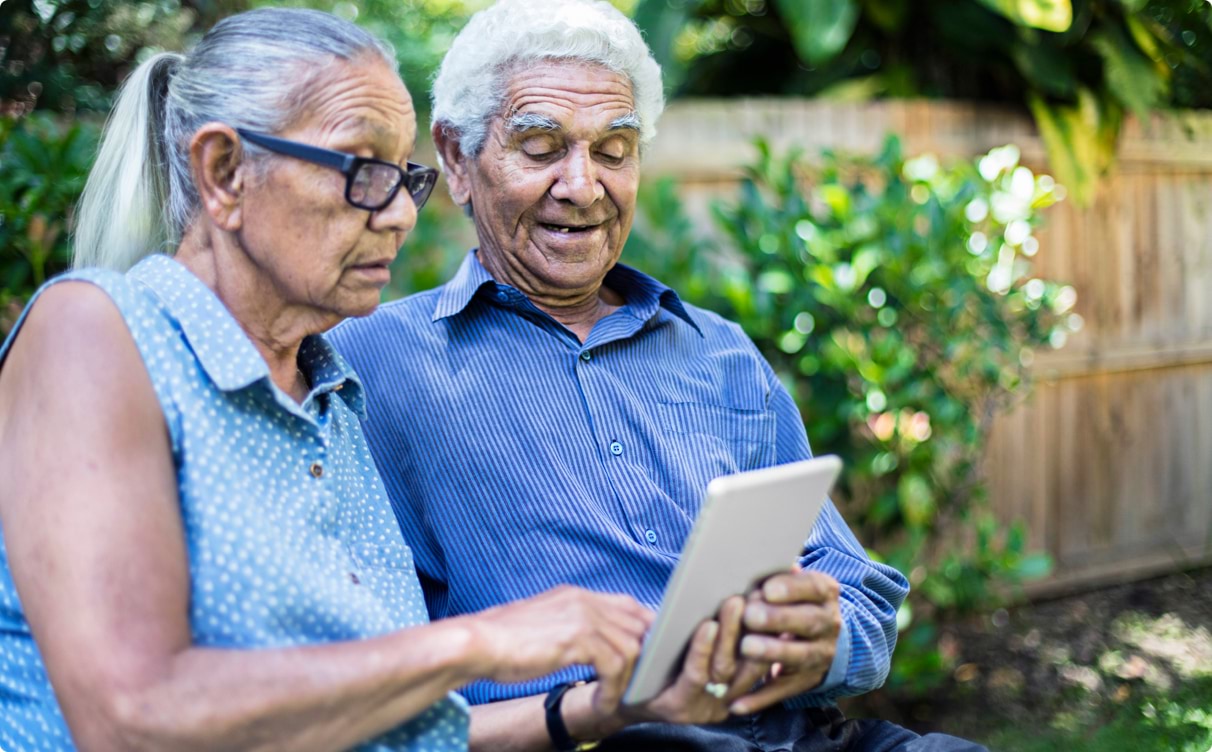 Elderly Indigenous couple sitting in the back yard, using an iPad together