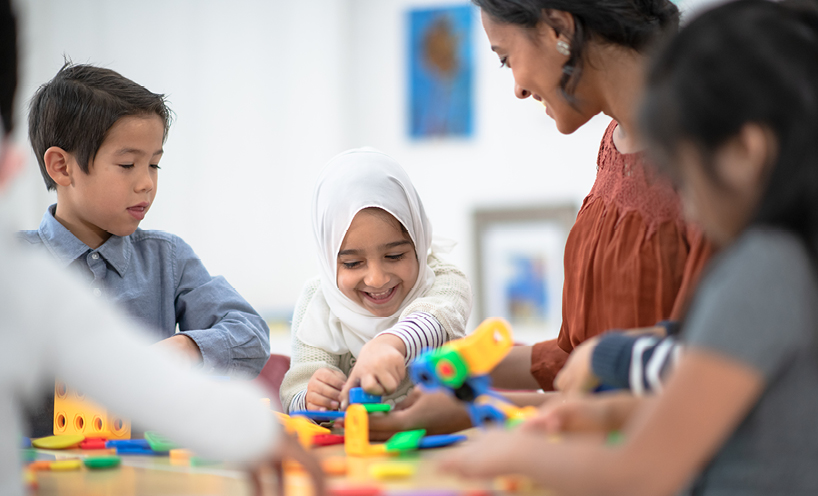 Young children sitting around a table smiling and playing with colour blocks