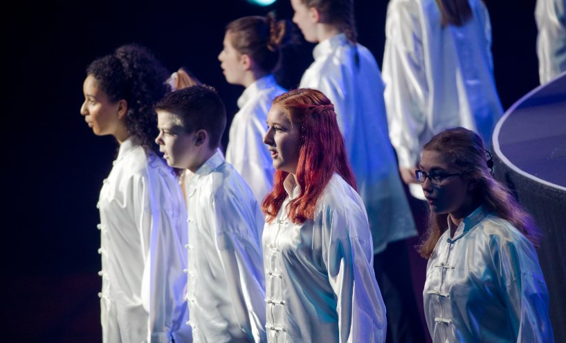 Small groups of students dressed in white, singing in a choir