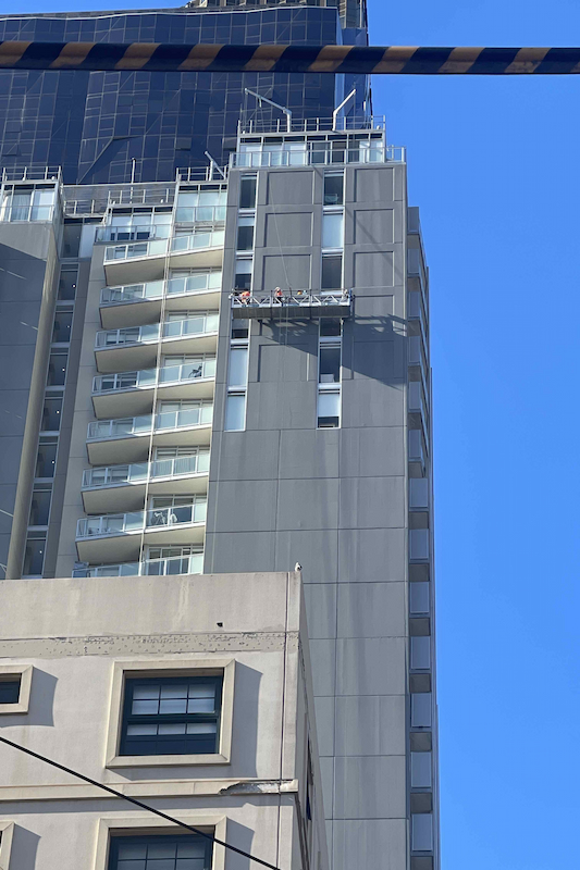 People working on a platform on the side of a high-rise building. 