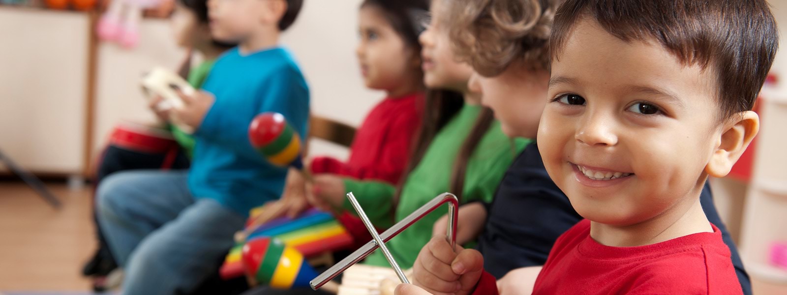 Child smiling playing triangle with other children in background