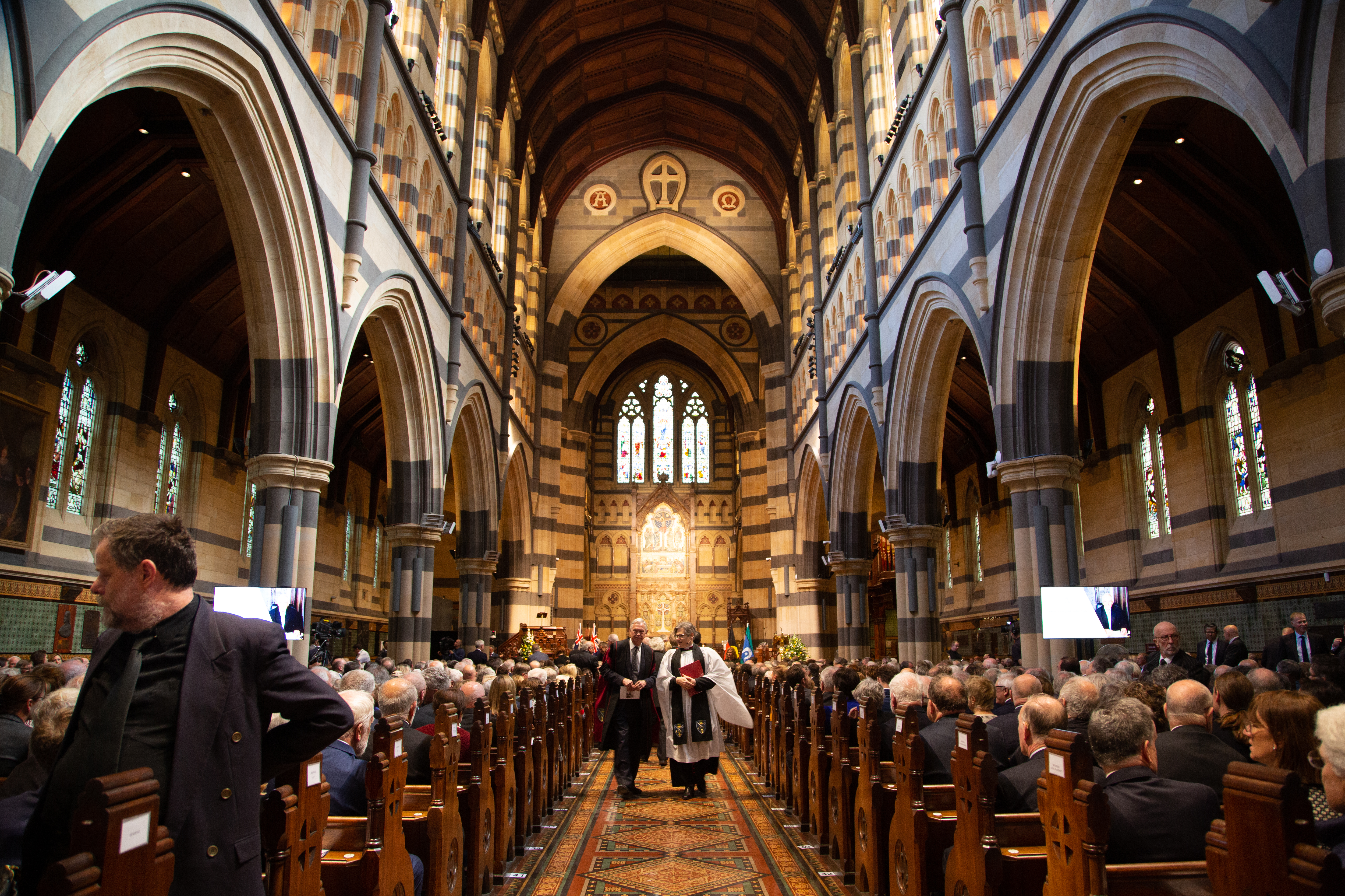 A reverend and another individual walk down the middle of a busy St Paul's Cathedral 