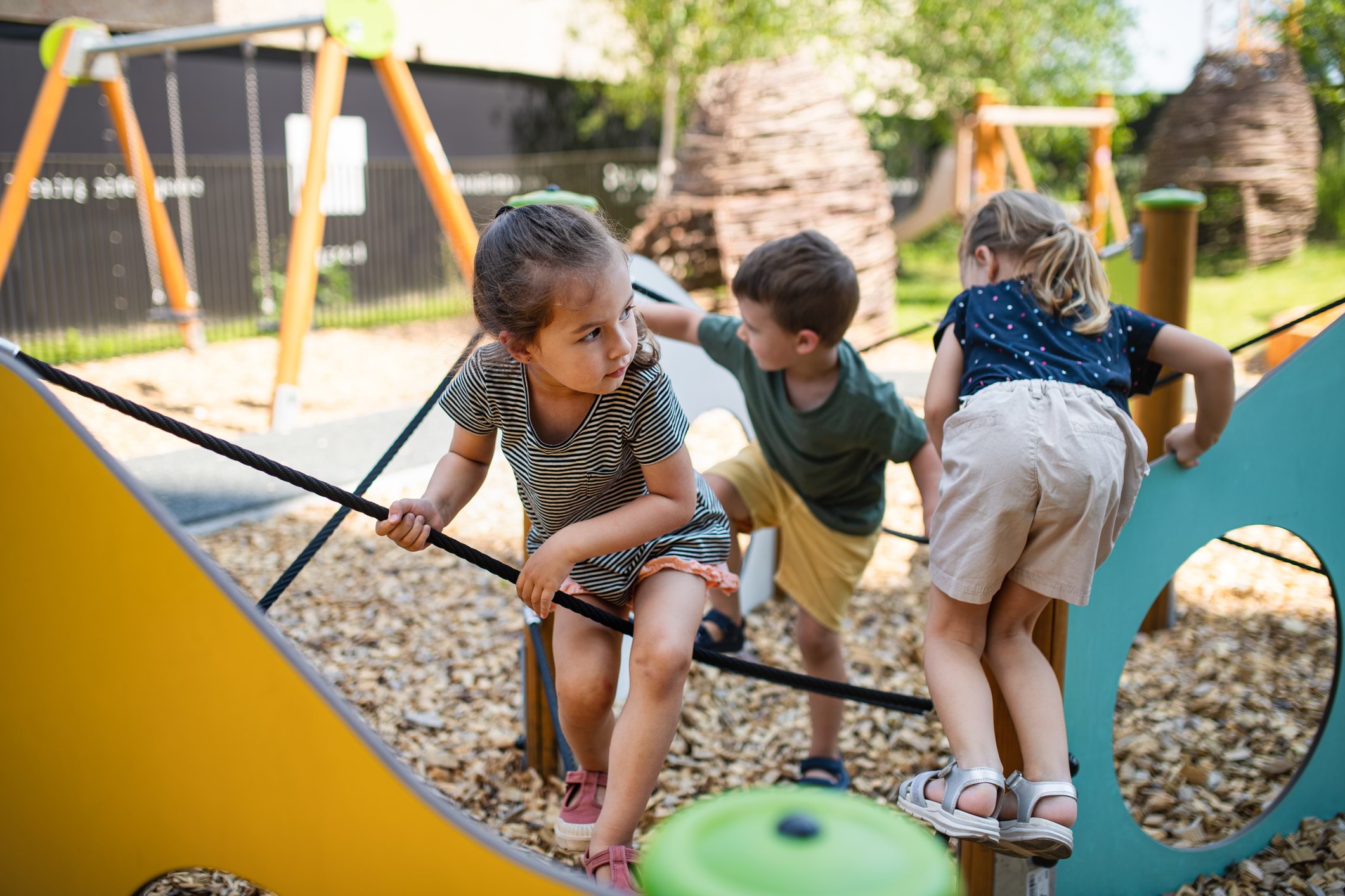 Three young children play together on an innovative, colourful school playground