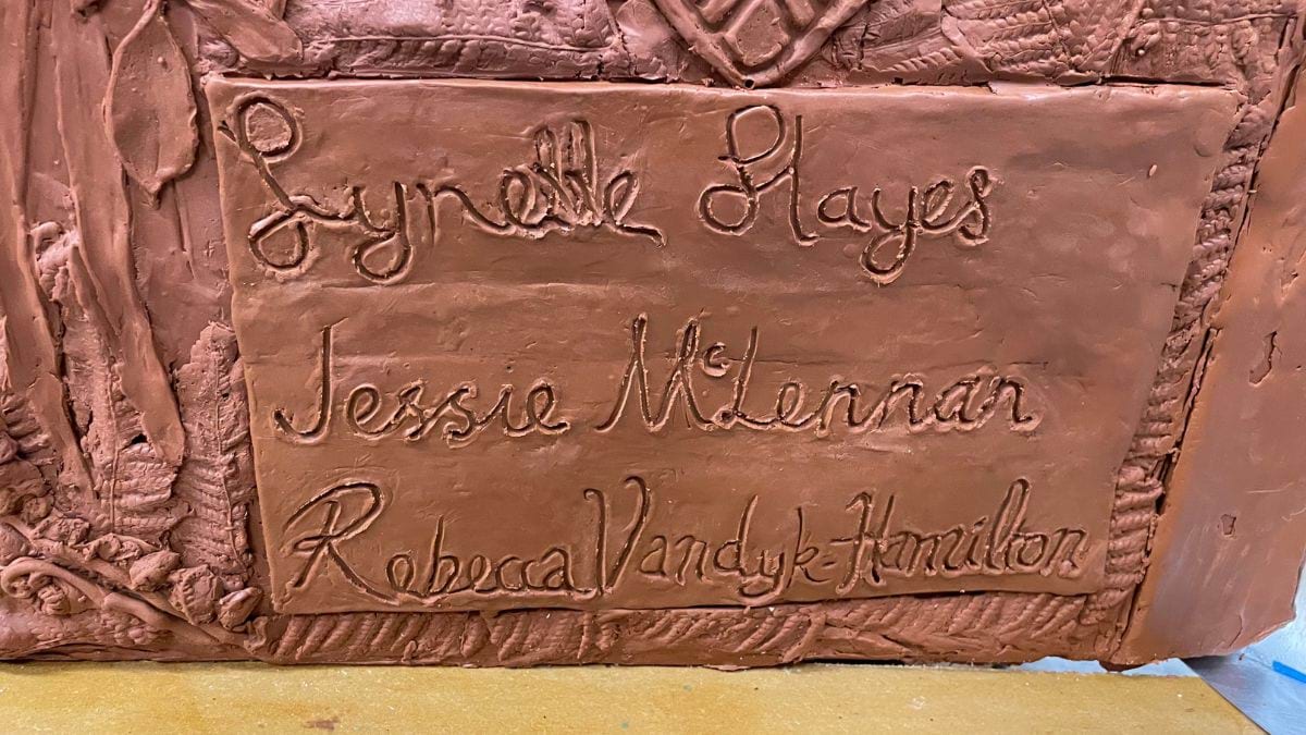 The plaque at the base of the sculpture with the artists names inscribed - Lynette Hayes, Jessie McLennan, Rebecca Vandyk-Hamilton. The border design on the plaque is by Lynette Hayes.