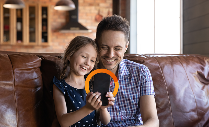 Father and daughter sitting on couch, smiling at tablet in front of them