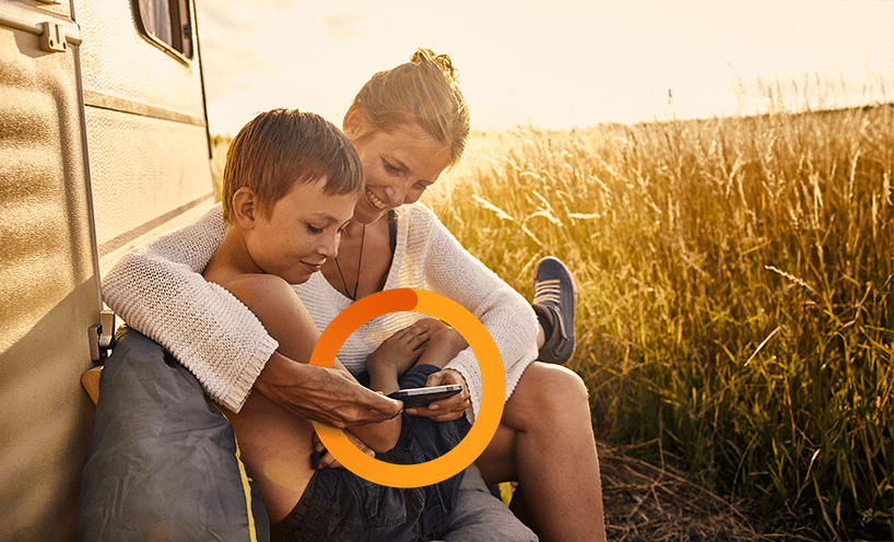 A mother and son are hugging, leaning against a white truck in a field of golden light, smiling and looking at phone