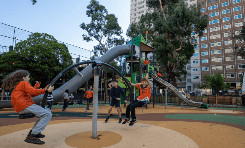 Multiple children playing in park in front of a large apartment