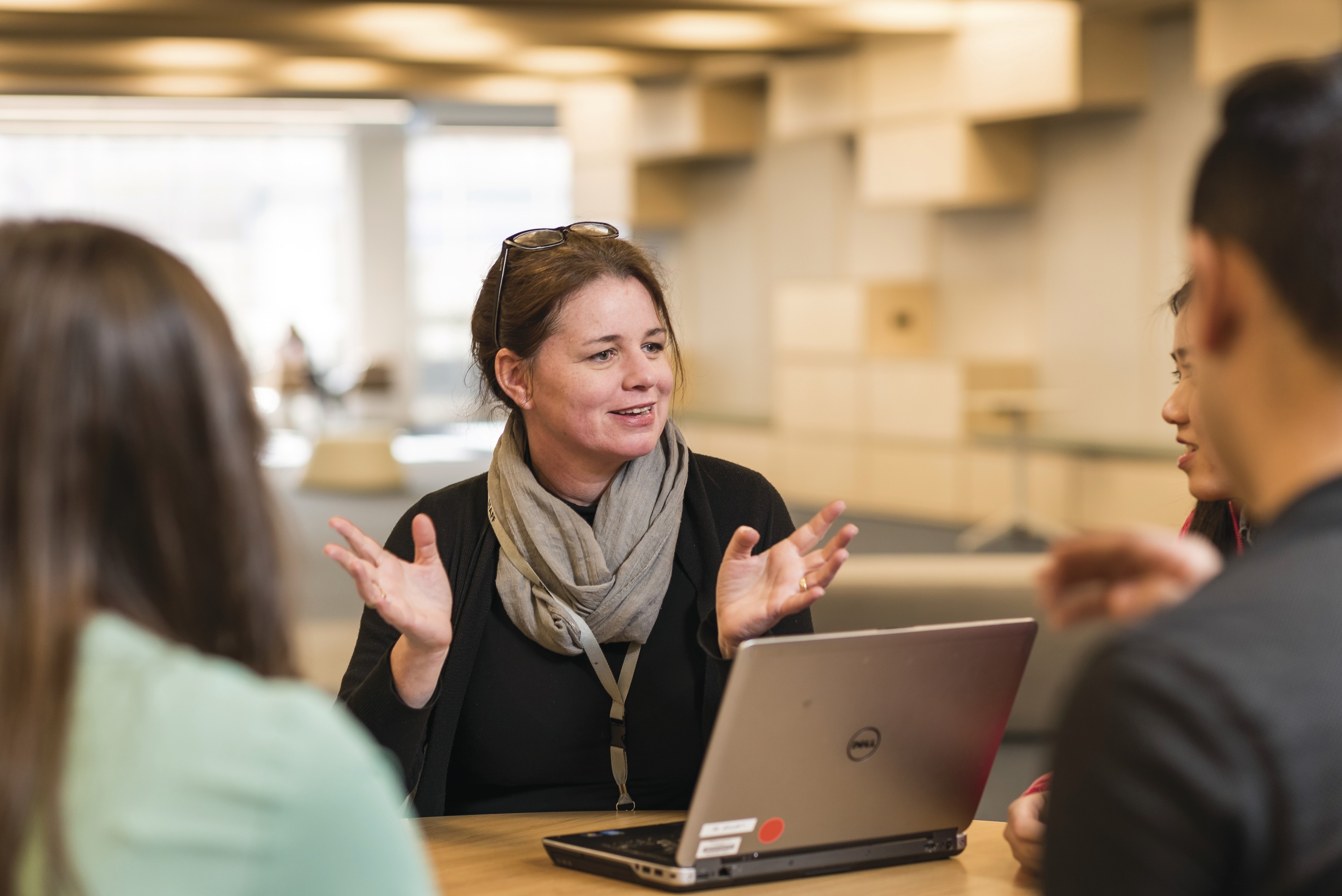 Person with hands open talking to other people and laptop in foreground.