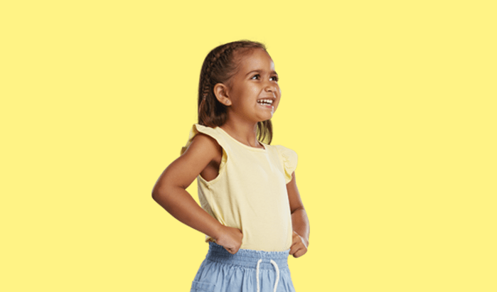 A young Koorie girl smiles with her hands on her hips, on a yellow background.