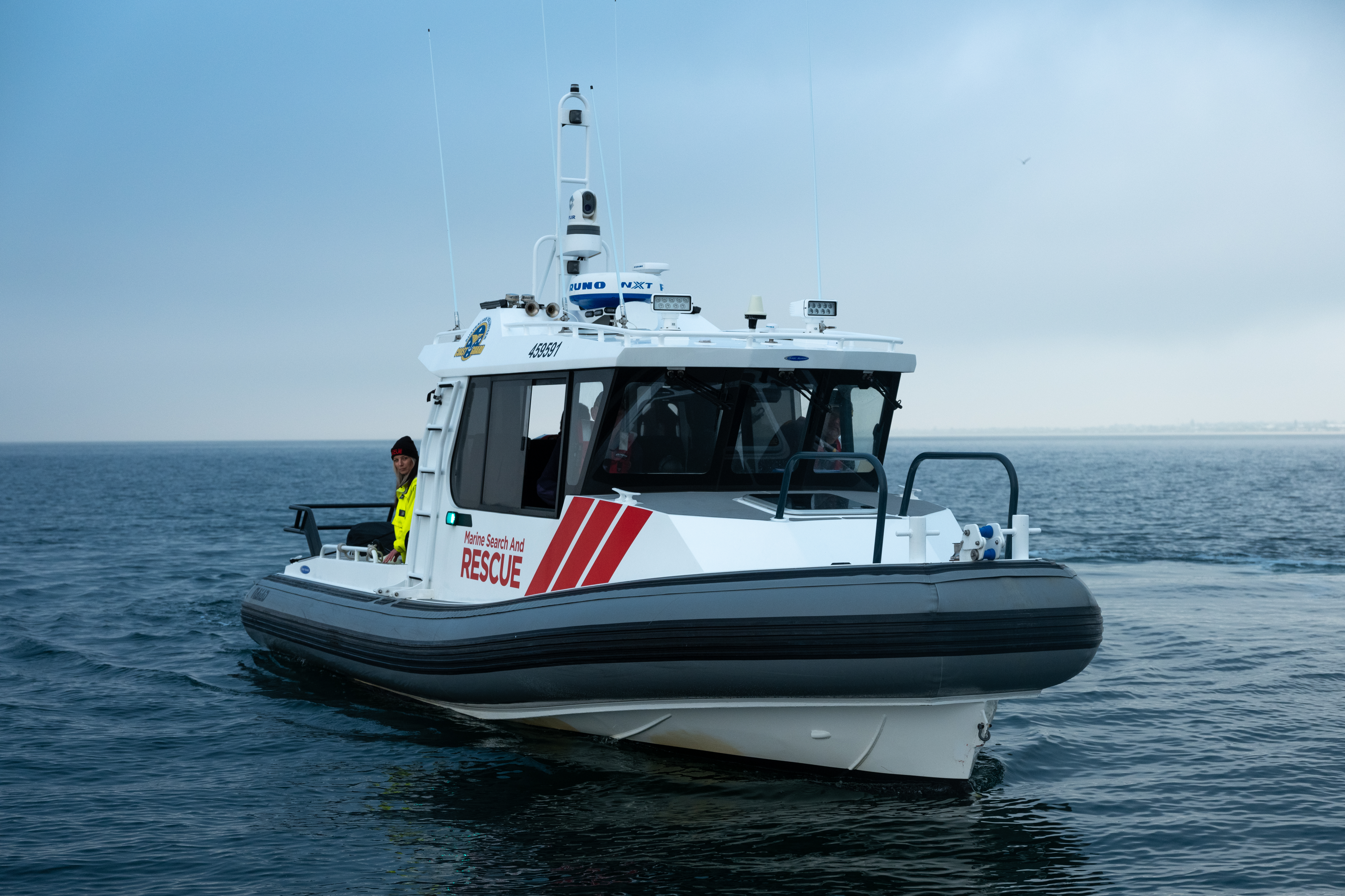 Image shows a boat on the water. The boat has Marine Search and Rescue on the side. There is a man standing toward the back of the boat. 