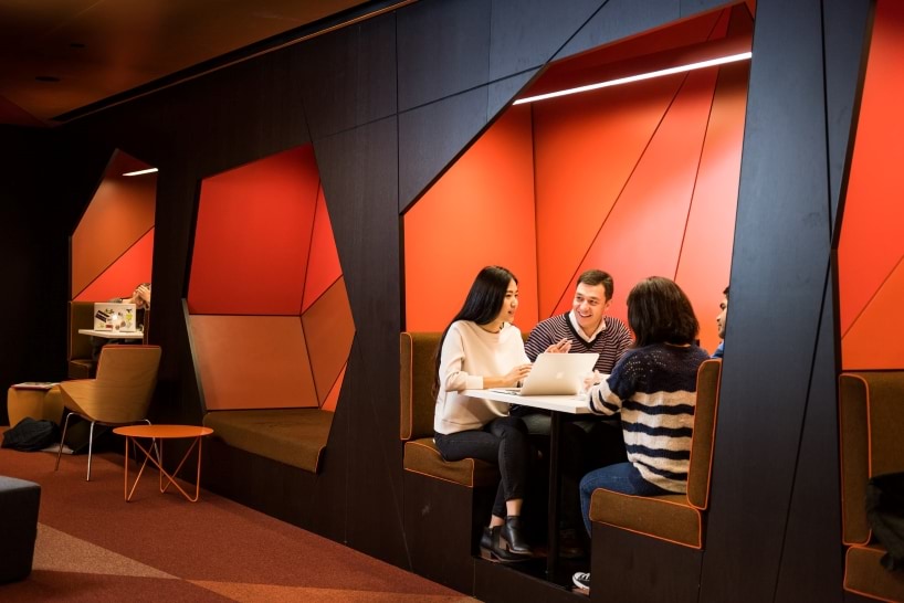 Students sitting in booth seating in a room with orange walls.