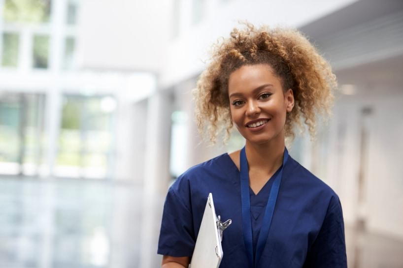 Person in scrubs holding clipboard smiling at the camera.