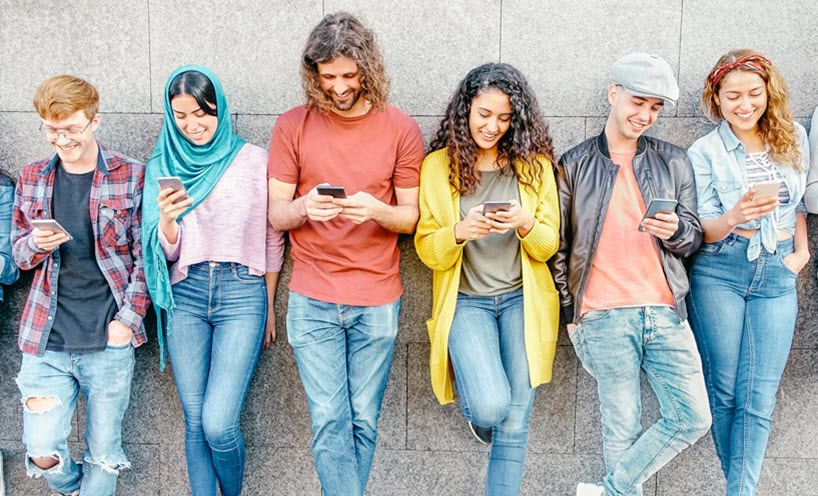 Group of young people looking at their hand held devices while leaning against a wall