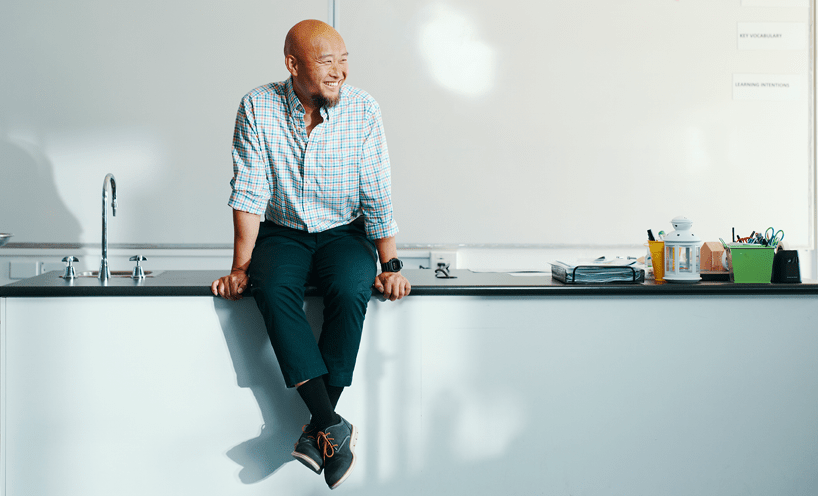 Male teacher sitting on a bench in front of a white board