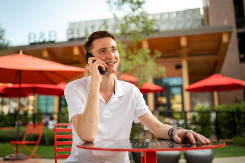 Person sitting outside at a table talking on the phone.