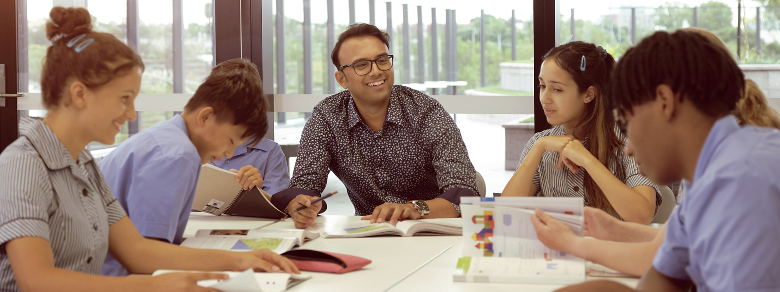 Male teacher sitting with high school aged students around a table.