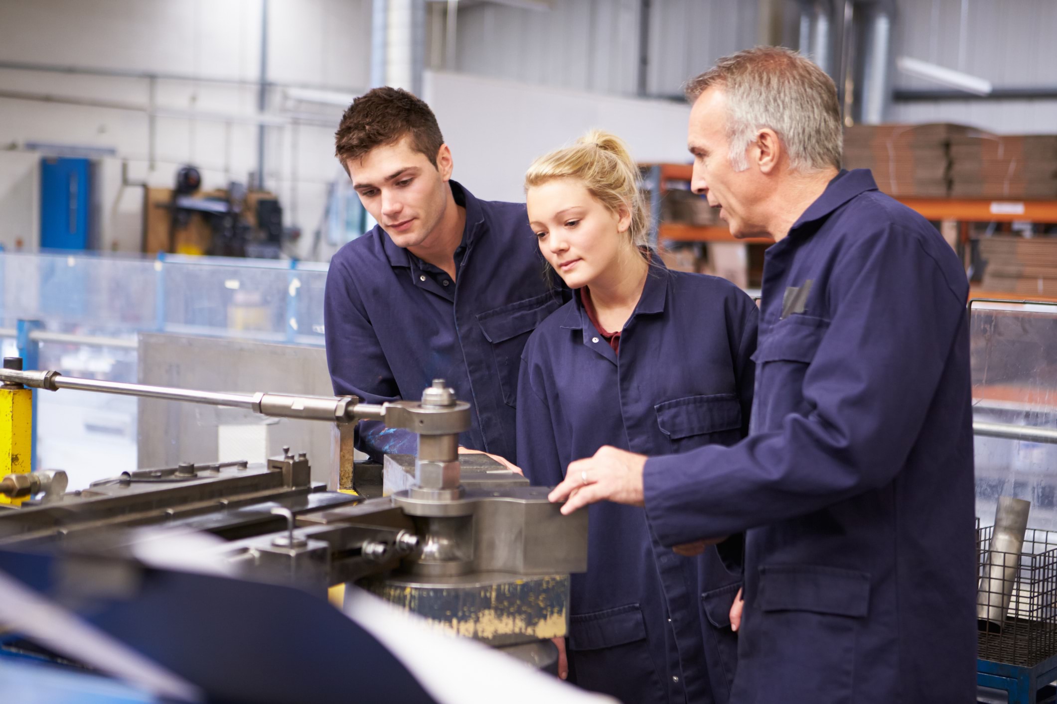 Skills Solutions Partnerships: 3 workers in blue trade workwear overalls looking at machinery with one older male instructing two younger workers