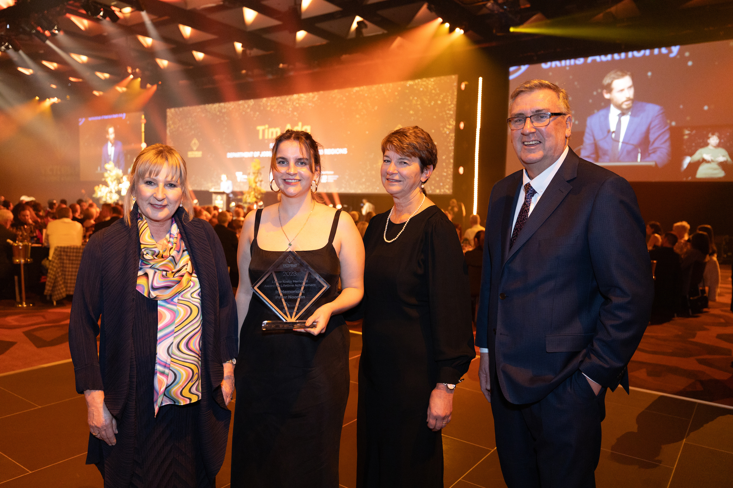 2023 Victorian Training Awards event with gala ceremony surrounds with Minister Gayle Tierney and Victorian Skills Authority Craig Robertson and two winners in between holding a trophy.