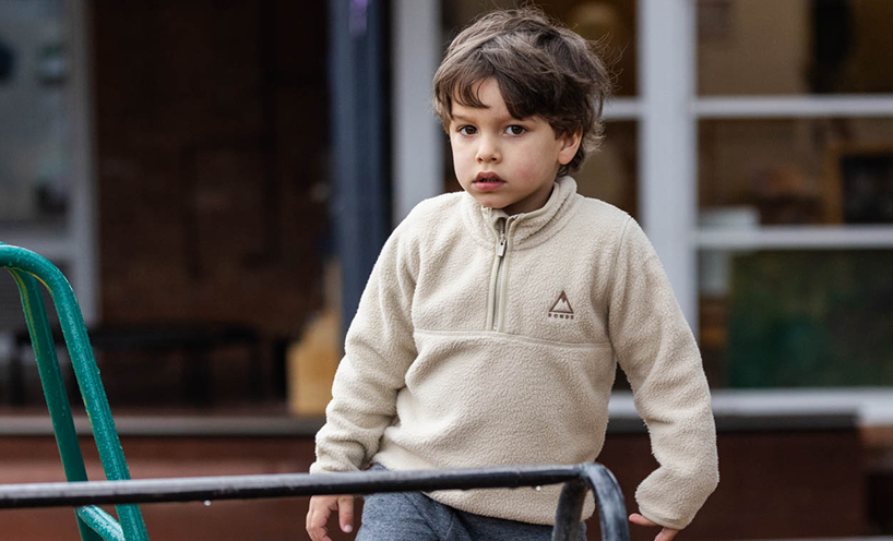 A kinder student is outside on on the play equipment. He wears a cream-coloured jumper and is looking towards the camera