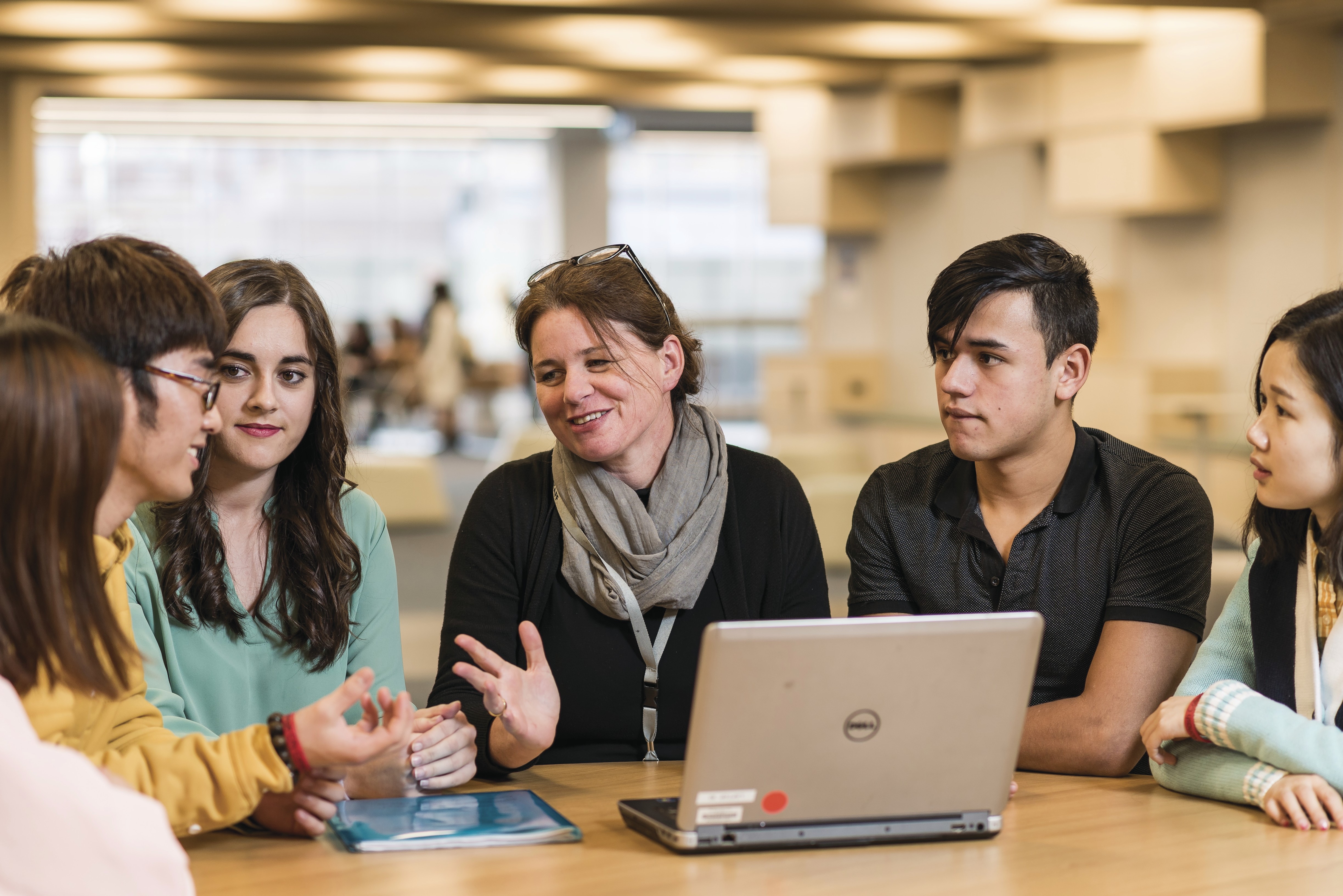 Group of diverse young people of mixed ages and appearances sitting around a table with a laptop talking.