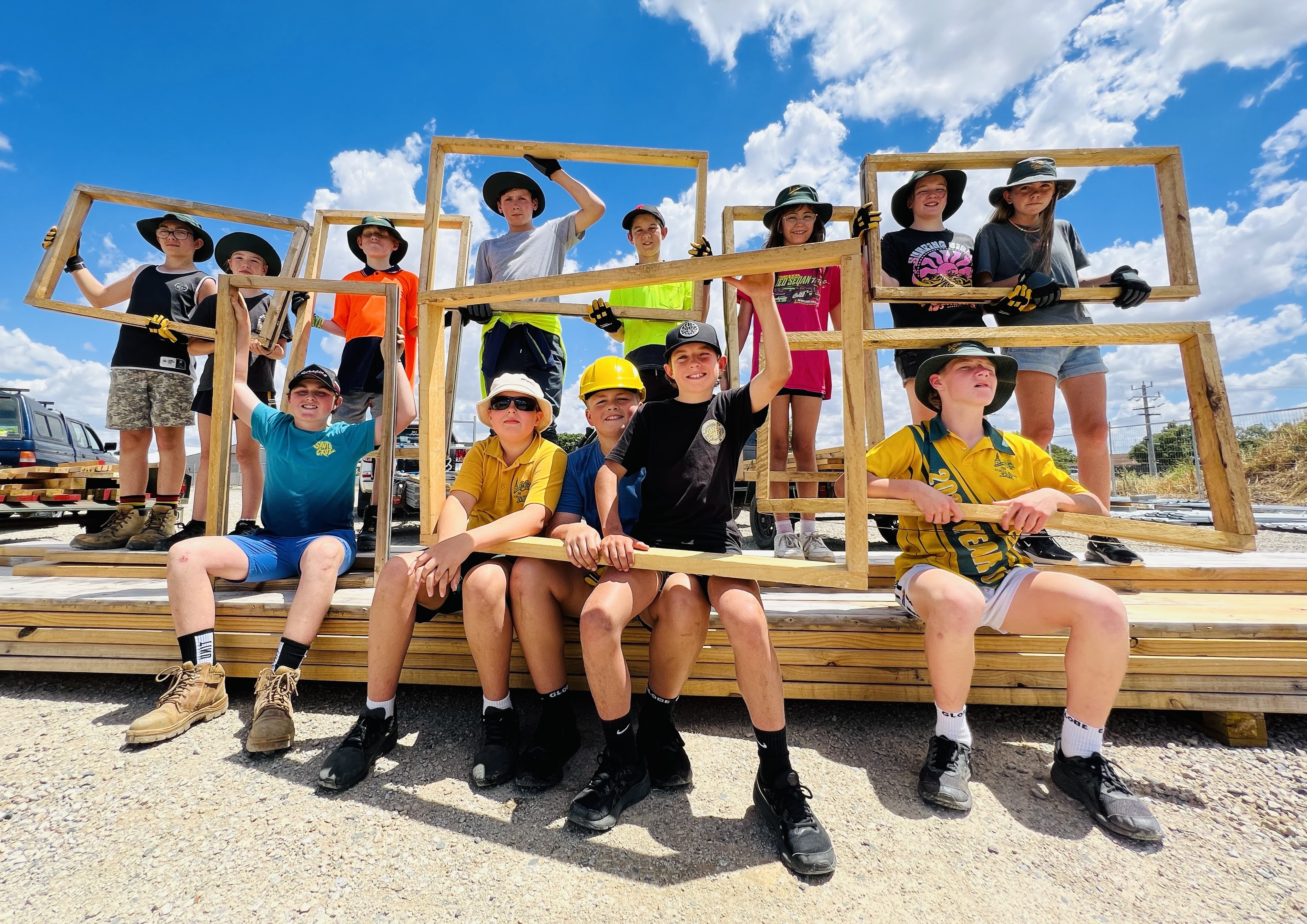 Echuca Primary School Hands on Learning program children sitting outside on top of building supplies and holding up wooden frames for their outside project