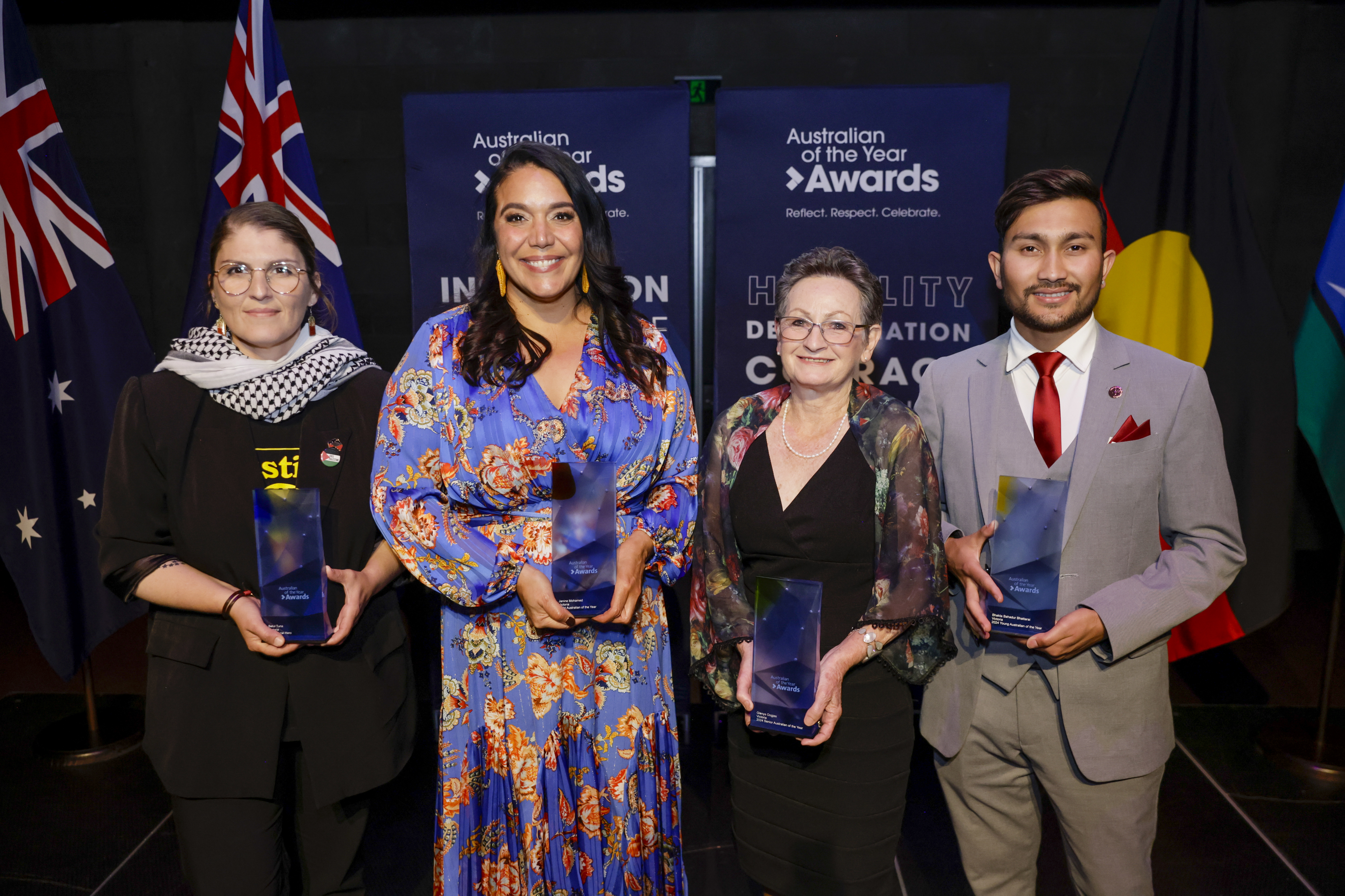 Four people stand near flags each holding an award