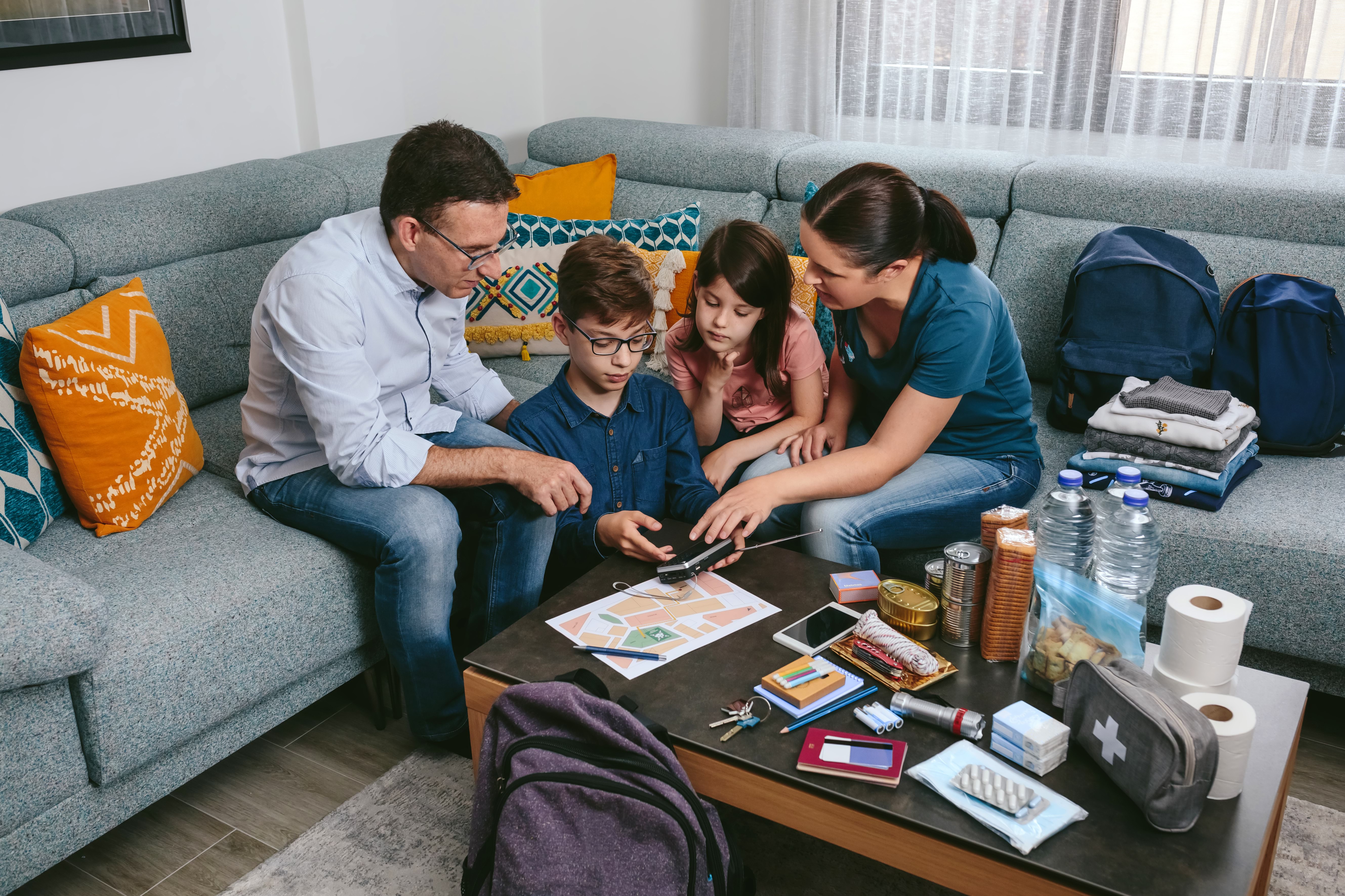 A fathher mother and two children sitting down in front of first aid kit, planner, phones and torch 