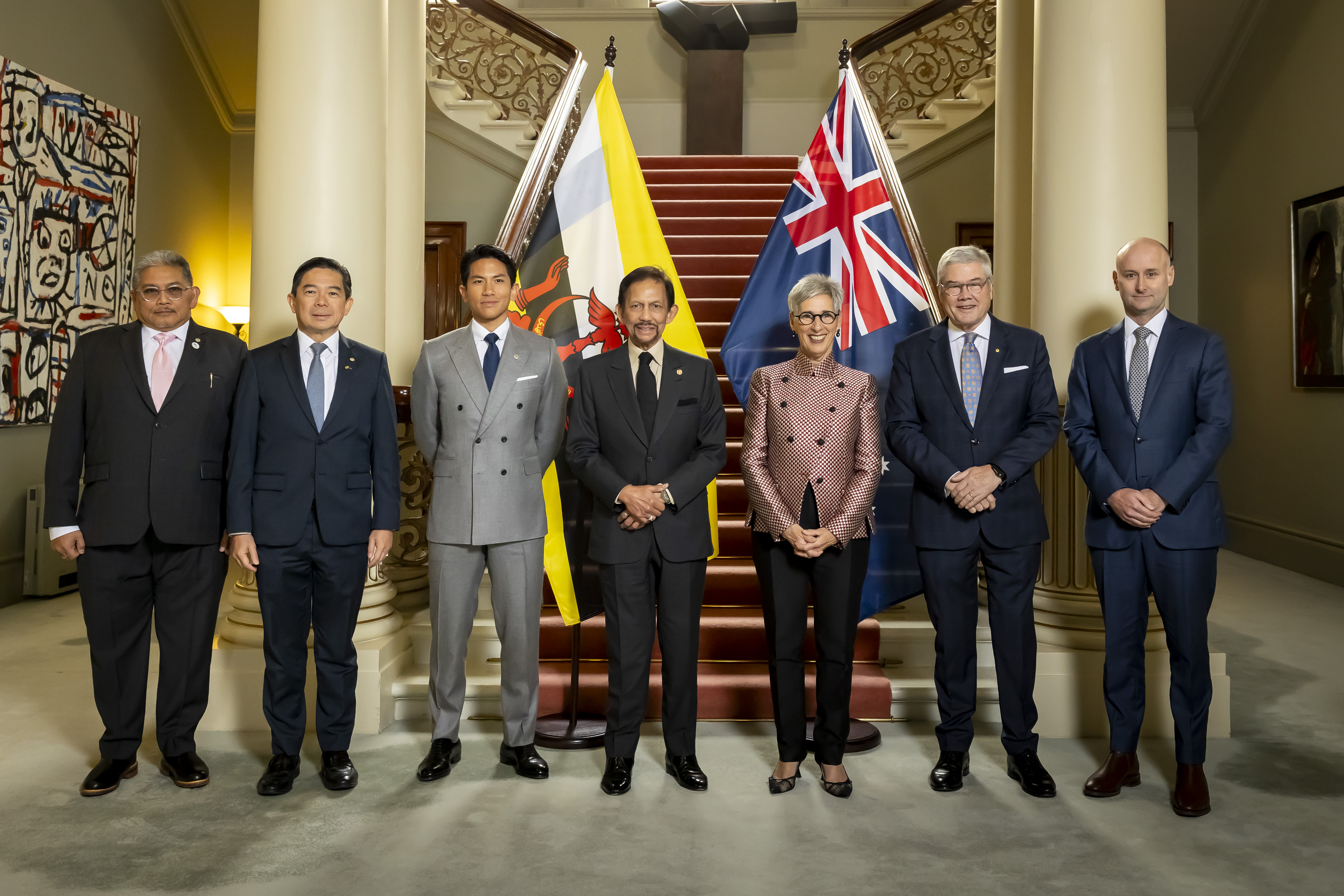 Seven people stand in front of the flags of Australia and Brunei