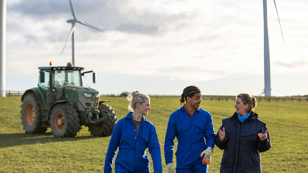 Three people in paddock with tractor and wind turbine