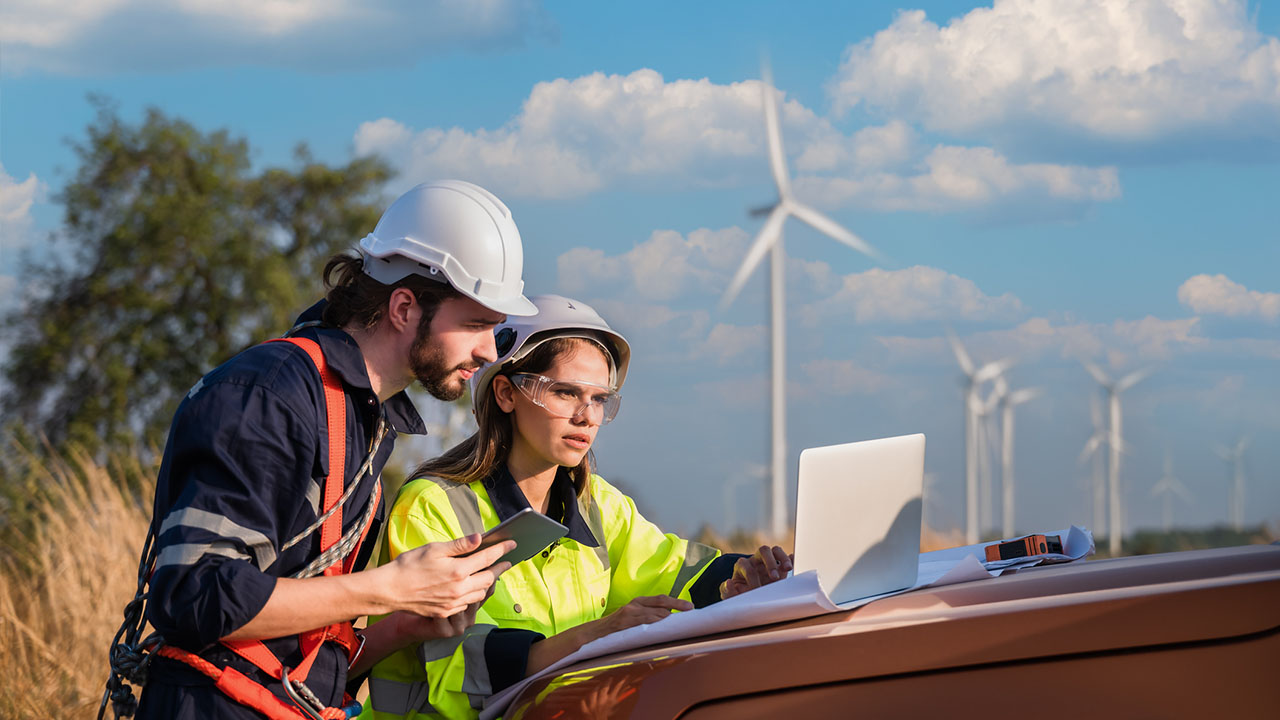 Two people working on laptop with wind turbines in background