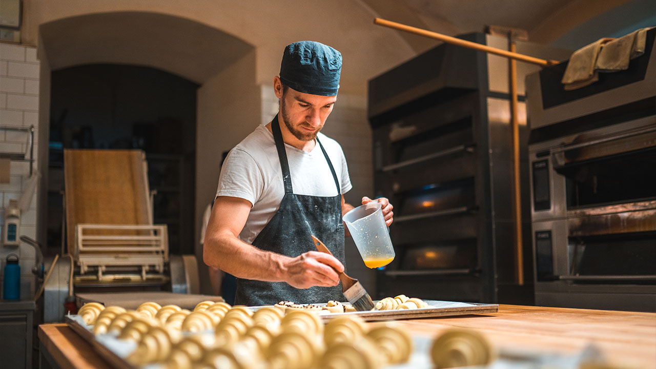 Artisan baker applying egg wash onto pastries