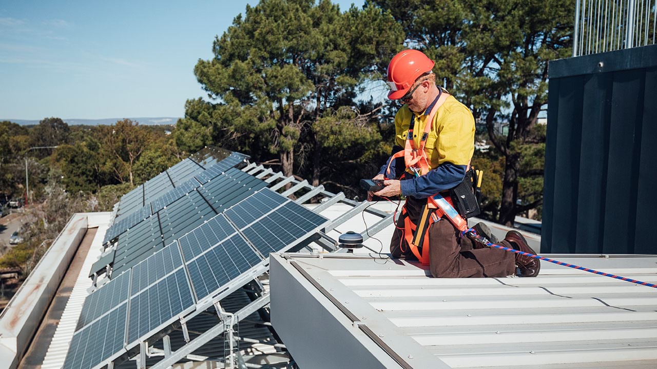 Person in safety equipment installing solar panels on rooftop