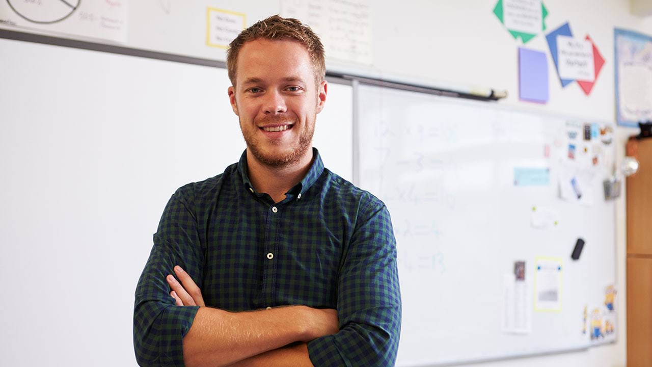 Teacher standing in front of a white board, looking at the camera