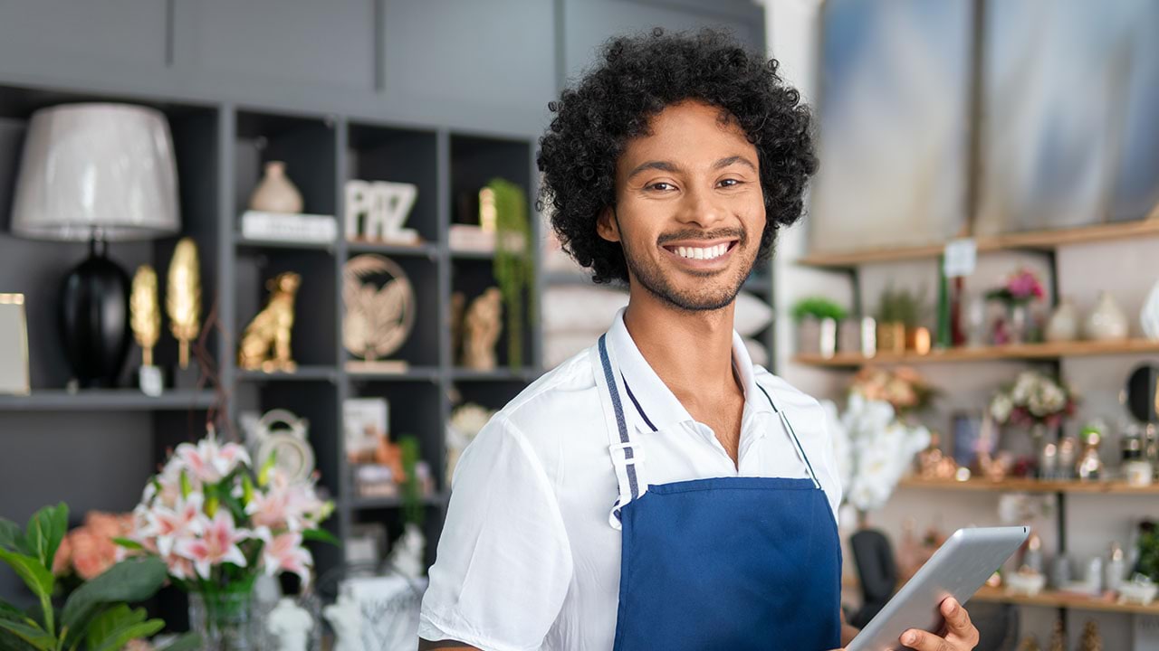 Person working in a shop holding a device, looking at the camera