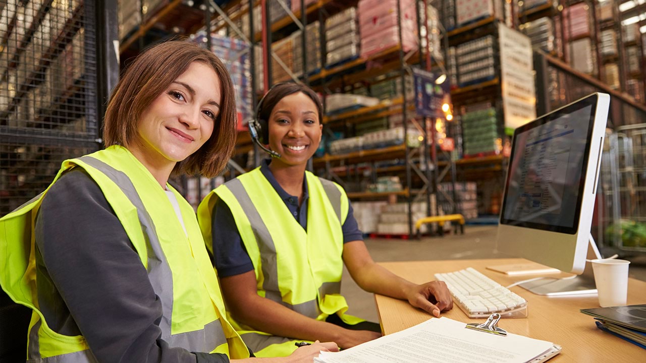 Two people wearing high-vis in warehouse working on a computer