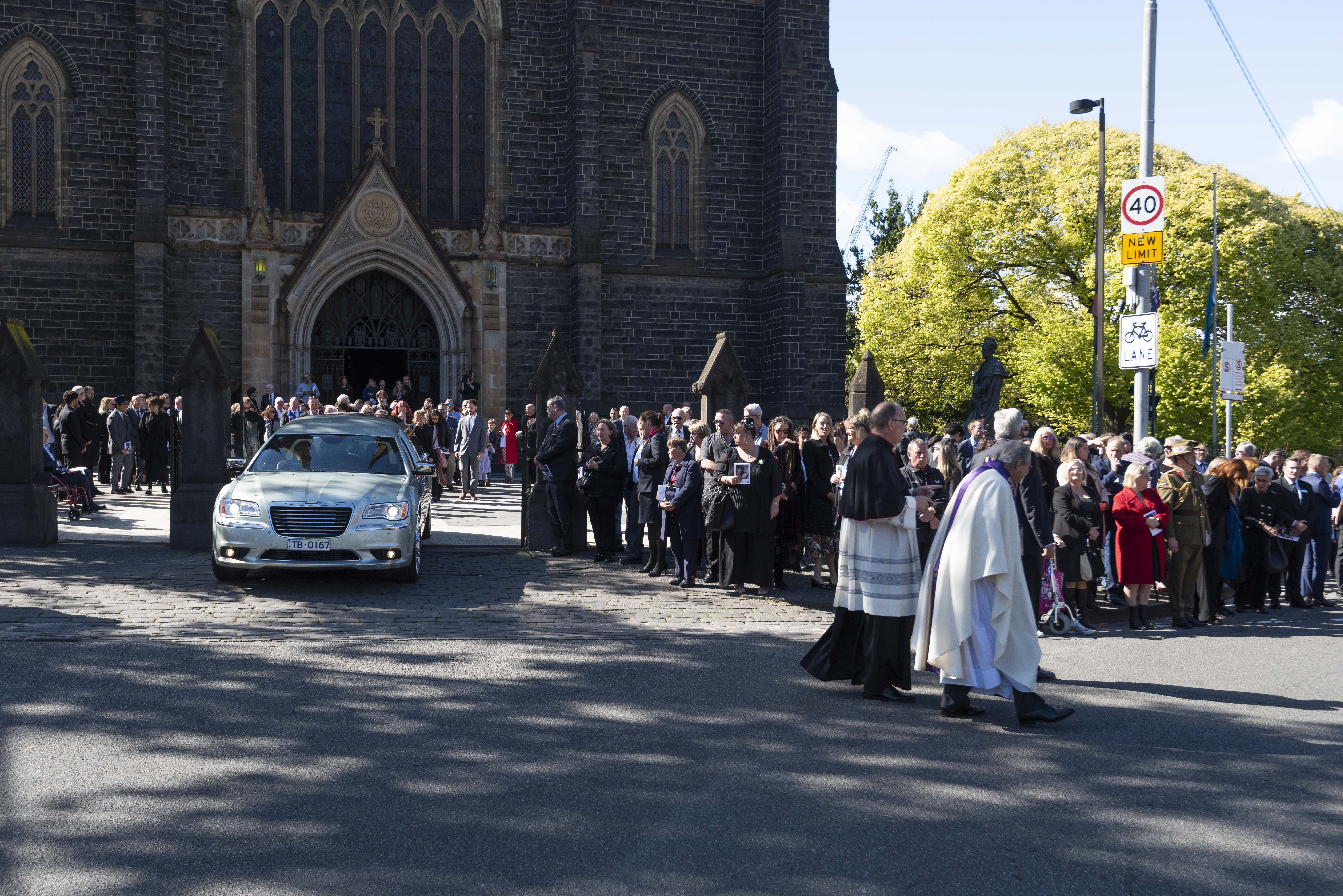 The Dean of St Patrick’s Cathedral and Father Joe Giacobbe lead Leslie Twentyman’s procession, followed by a hearse with the congregation lining the street and the Cathedral in the background. 