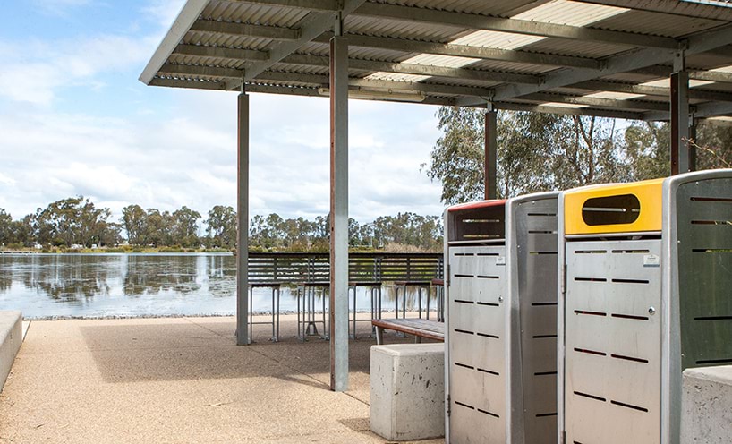 A barbecue area beside a lake, with waste and recycling bins in the foreground