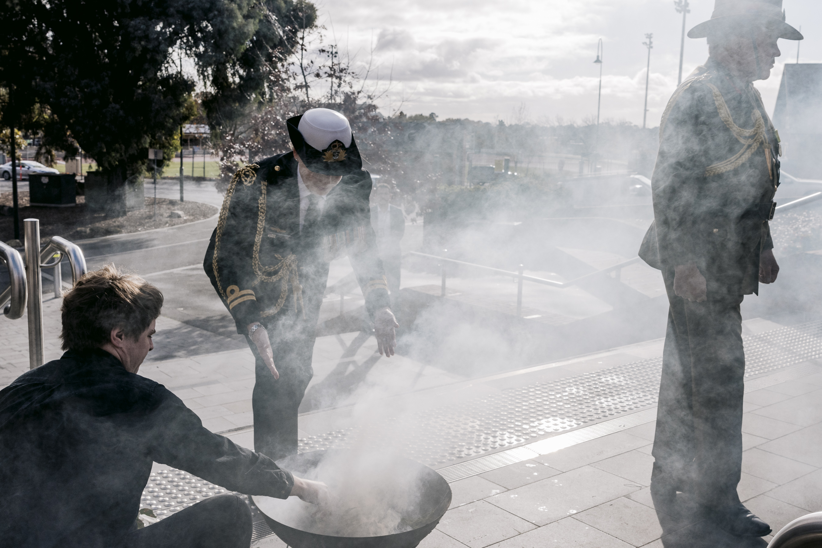 A person wearing an official uniform walks through smoke from a small fire pit. 