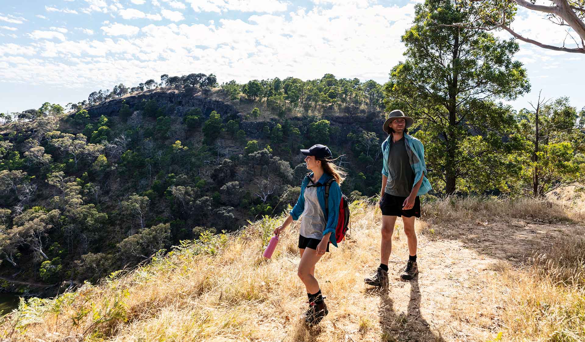 A young woman leading a man on a hilltop walk while admiring the scenery