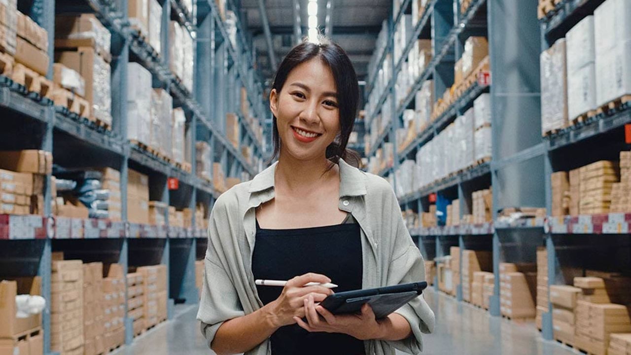 Person standing in warehouse holding a clipboard and pen