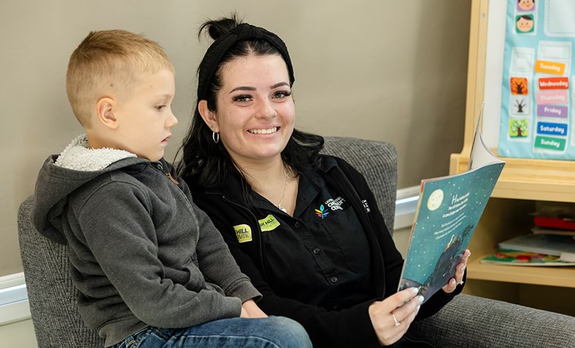 A woman and young child sit on an armchair reading a book.