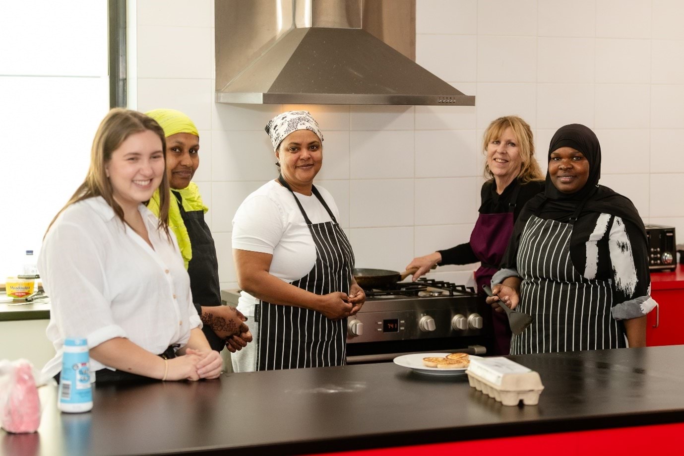 5 people standing in a kitchen, facing the camera and smiling