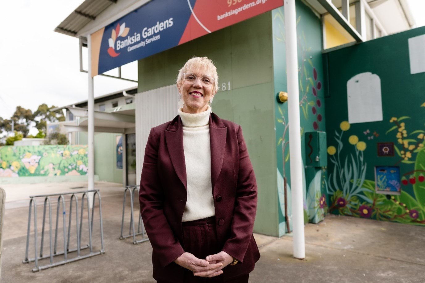 Gina Dougall portrait, standing in front of banksia gardens building and sign. 