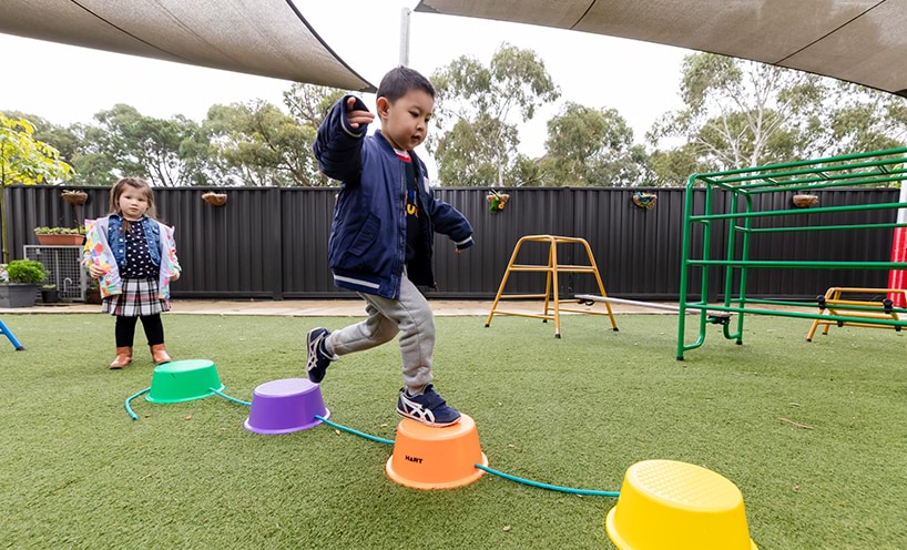 A young boy playing outdoors on plastic coloured buckets.