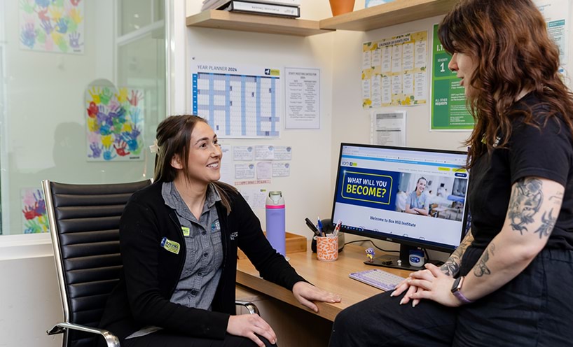 Two women chatting at an office desk.