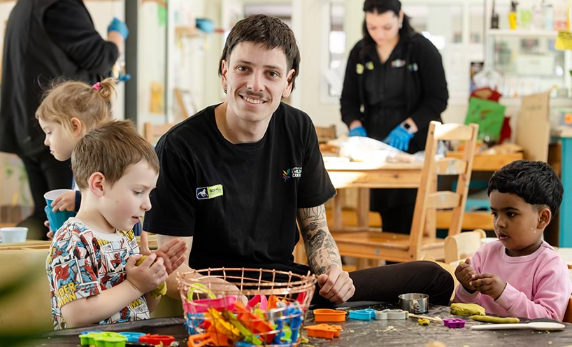 An early childhood professional sits with two children at a table, playing with Play-Doh.