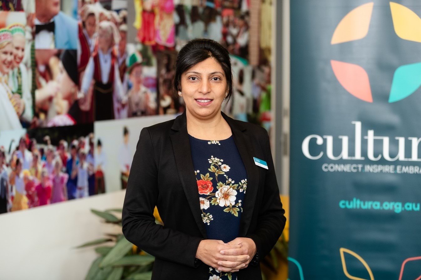 Sonia Nayyar standing portrait, wearing a floral top and black blazer, with cultura banner in the background. 