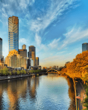 A view of a Melbourne river with a building towers in the background, a bridge, trees and a blue sky